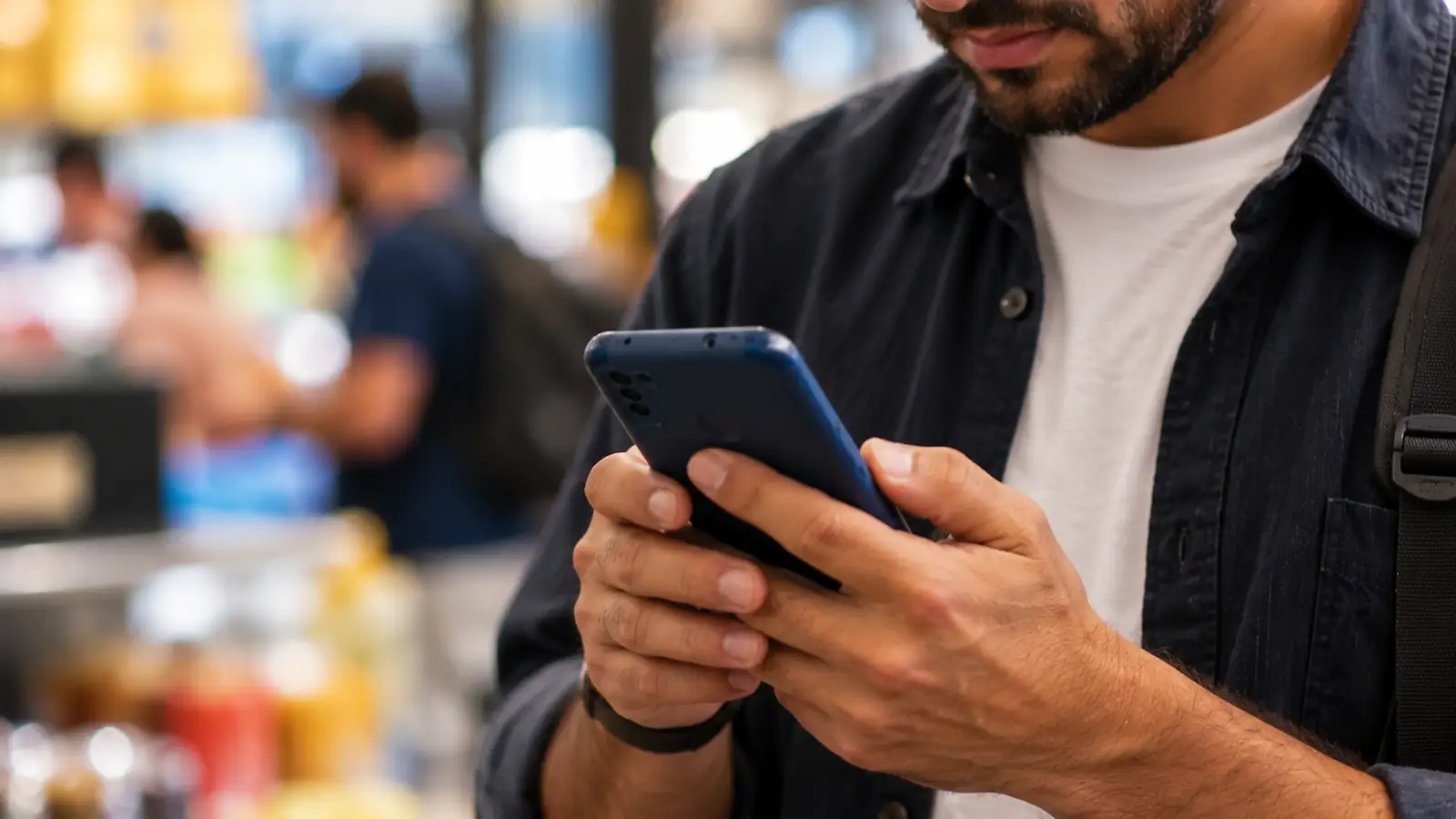 Homem olha o celular em local movimentado, cenário comum das ligações de telemarketing